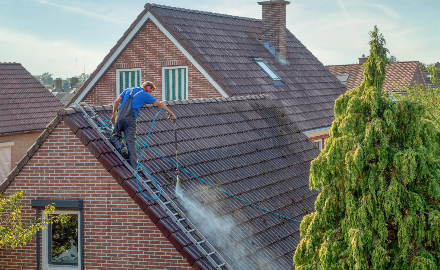 Ouvrier qui démousse une toiture en tuile à moyenne pression